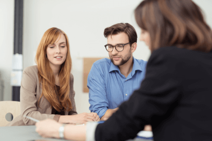 Broker making a presentation to a young couple showing them a document which they are viewing with serious expressions Broker making a presentation to a young couple showing them a document which they are viewing with serious expressions